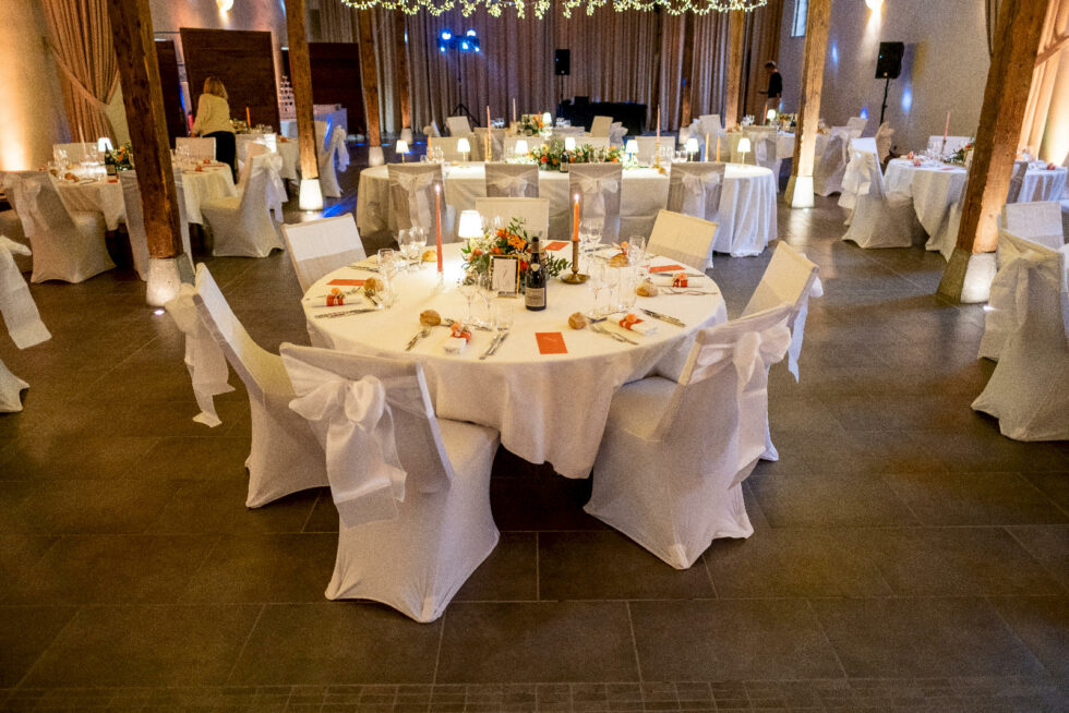 Aménagement de réception avec tables rondes nappées blanc et éclairage chaleureux dans une salle de mariage
