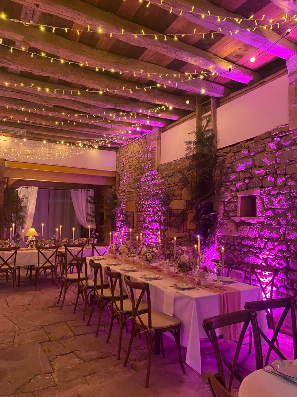Salle de mariage rustique en pierre avec guirlandes lumineuses et éclairage violet ambiance chaleureuse